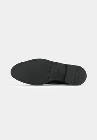 Semelle de chaussure noire avec un bout pointu, des coutures visibles et la marque "BOSS" embossée près de la voûte plantaire sur un fond uni.