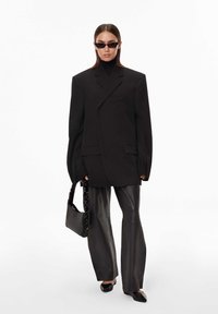 Nadrozměrné černé sako, přiléhavý černý rolák, černé kožené kalhoty a špičaté černé boty. Doplňky zahrnují černé sluneční brýle a kabelku.