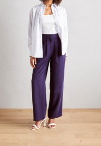 Wit en blauw gestreept overhemd met knopen, gecombineerd met marineblauwe, hooggetailleerde broek en witte sandalen met hak. Gladde stof en een ontspannen pasvorm.