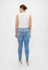 Light blue jeans with a slim fit, featuring back pockets and a high waist, worn with a white sleeveless top and light-colored shoes.