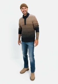 Gebreide trui in een bruin en marineblauwe gradient, met een kraagontwerp met knopen en opgerolde manchetten. Gepaarde met blauwe jeans en tan schoenen.