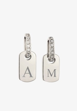 Silberne Creolen mit kleinen Kristallen und rechteckigen Silberanhängern, die mit den Buchstaben "A" und "M" graviert sind, auf weißem Hintergrund.