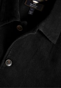 Black corduroy jacket with a textured surface, featuring a pointed collar and two metal buttons, displayed with care label visible.