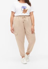 Béžové cargo kalhoty s elastickými manžetami, šňůrkou v pase a bočními kapsami. Spárovány s bílým tričkem s barevným abstraktním designem.
