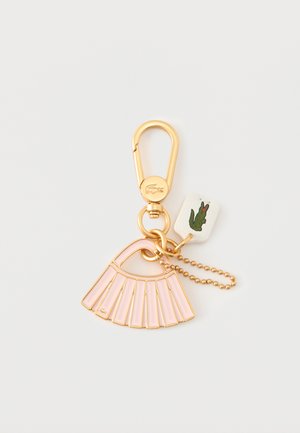 Guldfarvet nøglering med en pink vifteformet charm, en perlende kæde og et lille hvidt mærke med et grønt krokodillelogo.