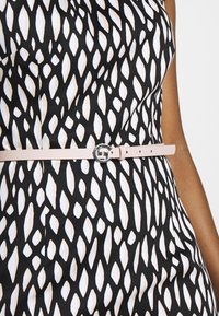 Robe à motifs noir et blanc avec des formes de feuilles irrégulières, cintrée à la taille par une fine ceinture rose clair avec une boucle argentée.