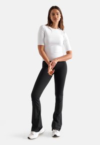 Hvit, tettsittende kortermet topp kombinert med svarte flagrende leggings; begge plaggene har glatt, elastisk stoff og et enkelt design.