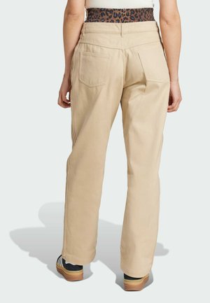 Beige wijde broek met een hoge taille en achterzakken, met contrasterende stiksels. Gemaakt met zwarte schoenen en een luipaardprint tailleband.