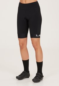 Zwarte fietsshorts met een gevoerde zitting en hoge tailleband. Heeft een logo op het been en zijn glad met een aansluitend ontwerp. Draagt met zwarte sokken en schoenen.