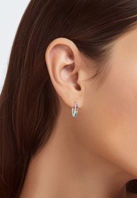 Petite boucle d'oreille en argent avec des pierres précieuses multicolores disposées le long du bord avant, portée sur l'oreille d'un mannequin sur fond neutre.