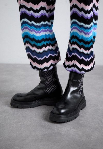 Botoși negri din piele, la gleznă, cu o talpă masivă și accente cu model zigzag în toc. Purtați cu pantaloni tricotati colorați, cu model zigzag.