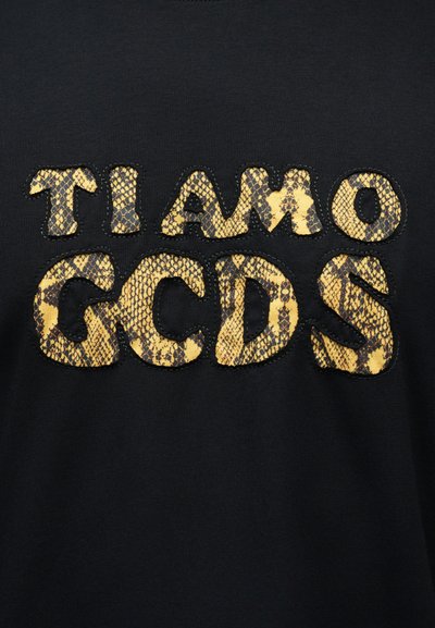 Schwarzer Stoff mit auffälligen gelben und schwarzen Buchstaben im Schlangenhautmuster, die "TI AMO GCDS" auf der Oberfläche aufgestickt sind.