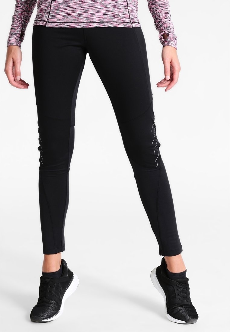 Schwarze Sportleggings mit schmalem Schnitt, glatter Textur und reflektierenden Akzenten an den Seiten. Kombiniert mit schwarzen Sneakers.