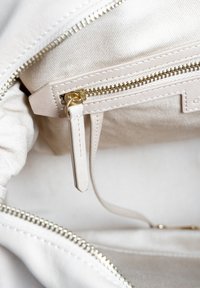 Beige stoffen interieur van een tas met een ritsvak. De rits heeft metalen hardware en er is een stoffen label aan bevestigd.