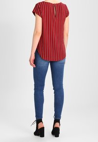 Červeně pruhovaná blůza s krátkým rukávem a klíčovou dírkou na zadní straně, spárována s modrými skinny džíny a černými kotníkovými botami na podpatku.