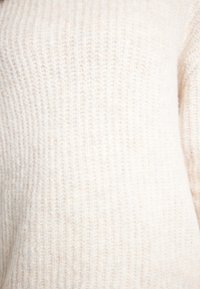 Ljus beige ribbad tröja, tillverkad av mjukt tyg med en strukturerad yta. Har vertikala linjer och en mysig känsla.