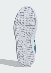 Vit gummisula på en sneaker med texturerat fiskbensmönster, med en turkos ovandel som har tre vita ränder och mjukt tyg.