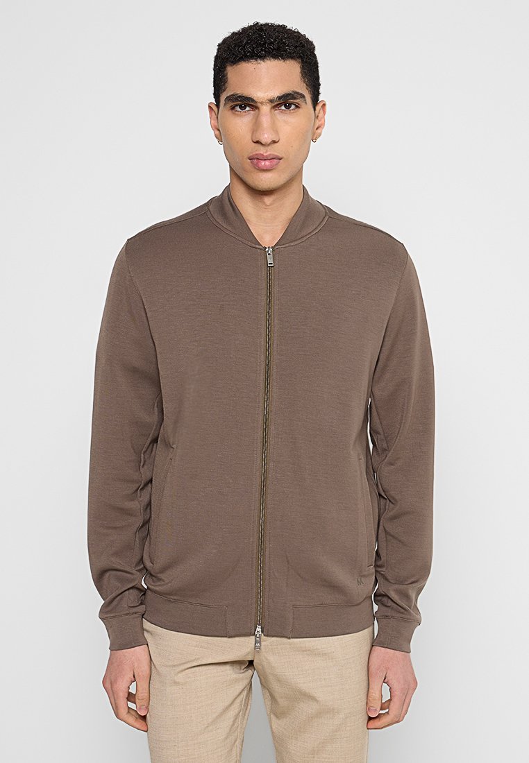 Brązowa kurtka bomberka na zamek błyskawiczny z prążkowanym kołnierzem, dwoma przednimi kieszeniami i gładkim, lekkim materiałem. Posiada metalowy zamek błyskawiczny.