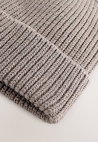 Cappellino lavorato a maglia in grigio chiaro con texture a coste. Presenta un risvolto piegato per maggiore calore. Realizzato con filato spesso. Leggero e accogliente.