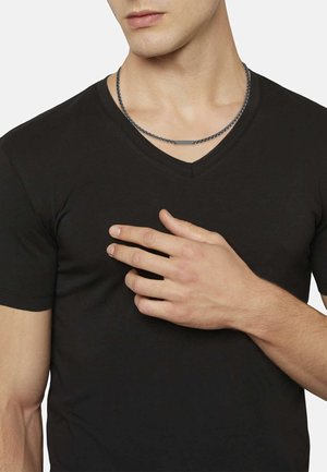 Schwarz V-Ausschnitt T-Shirt mit kurzen Ärmeln, glatte Textur, getragen von einer Person, die eine Hand auf der Brust hat und eine Kettenhalskette sichtbar ist.