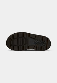 Semelle de chaussure en caoutchouc noir présentant une surface texturée avec plusieurs motifs de crampons et rainures pour une meilleure traction. Logo embossé au centre.