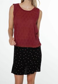 Top senza maniche bordeaux con un motivo testurizzato, abbinato a una gonna nera con piccole decorazioni floreali e orlo arricciato.