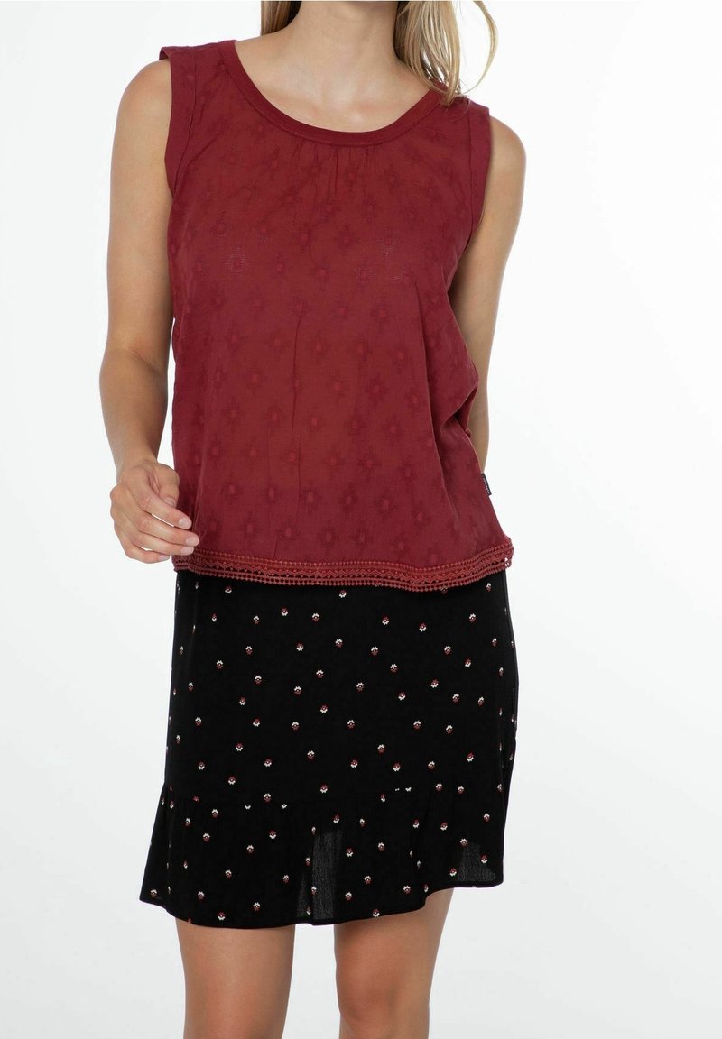 Top senza maniche bordeaux con un motivo testurizzato, abbinato a una gonna nera con piccole decorazioni floreali e orlo arricciato.