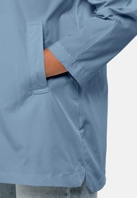 Lichtblauwe jas met een gladde, matte afwerking. Beschikt over een zijzak en detaillering bij de mouwnaad. Casual, ontspannen pasvorm.