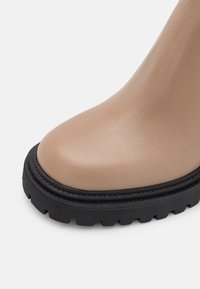 Bottines beiges avec une tige en cuir texturé et une semelle en caoutchouc noire épaisse. Bout rond avec des détails de couture contrastés.