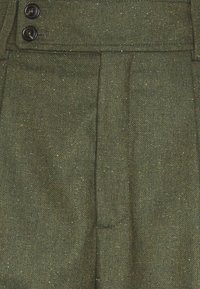 Zielono-oliwkowe spodnie wykonane z fakturowanej tkaniny w wzór muszki, z dwoma czarnymi guzikami i widocznymi fałdami z przodu.