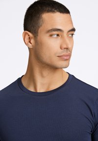 Granatowa bawełniana koszulka z okrągłym dekoltem, krótkimi rękawami oraz gładką fakturą. Zbliżenie na rysy twarzy modelki.