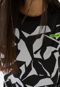 Svart kortärmad skjorta med ett vitt abstrakt mönster. Inkluderar en framträdande grön logga "FIRE + ICE" på bröstet. Nätstruktur.