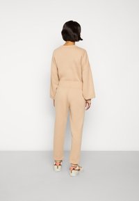 Sweatshirt oversized bege e calças de jogging combinando. Tecido macio, ajuste descontraído, cintura elástica e punhos canelados. Ténis desportivos completam o visual.