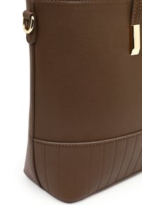 Brown leather handbag detail with gold-tone hardware, vertical stitching along the bottom, and a side strap with a metal ring.