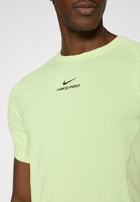 Πράσινο αθλητικό μπλουζάκι με κοντά μανίκια από ελαστικό ύφασμα. Διαθέτει το λογότυπο Nike Pro σε μαύρο, λεπτομέρειες από δίχτυ στα μανίκια και στρογγυλή λαιμόκοψη.