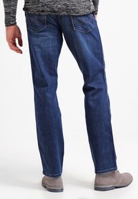 Mörkblå denimjeans med rak skärning, utrustad med två bakfickor med sömnadsdetaljer, bärs med grå ankelstövlar.