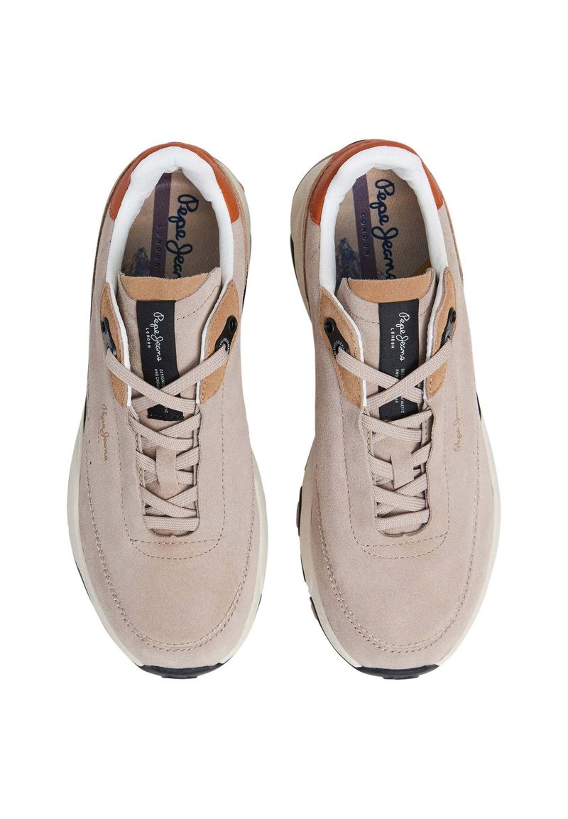 Zapatillas de ante beige con suela de goma blanca, diseño de lazada central y acentos de cuero marrón en el talón. El forro interior es blanco.