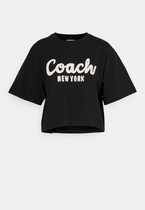 Schwarzes, kurzes T-Shirt aus Baumwolle mit großen weißen "Coach New York"-Schriftzug auf der Vorderseite und kurzen Ärmeln. Glatte Textur.
