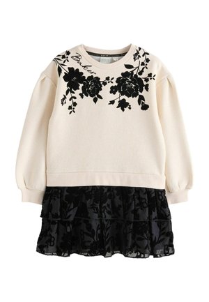 Langärmliges cremefarbenes Sweatshirt mit schwarzem Blumendruck und Puffärmeln, kombiniert mit einem schwarzen, gerafften Rock aus transparenter Stoff.