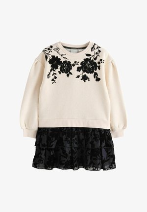 Ilgām piedurknēm krēmkrāsas sporta krekls ar melnu ziedu izdruku un puffed piedurknēm, kārtots ar melnu volānu svārku, kas izgatavots no caurspīdīgas auduma.