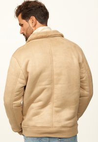 Beige Kunstlederjacke mit einem weichen, mit Fell gefütterten Kragen. Verfügt über gerippte Bündchen und Saum sowie eine gesteppte Naht auf der Rückseite. Lässiges Design.