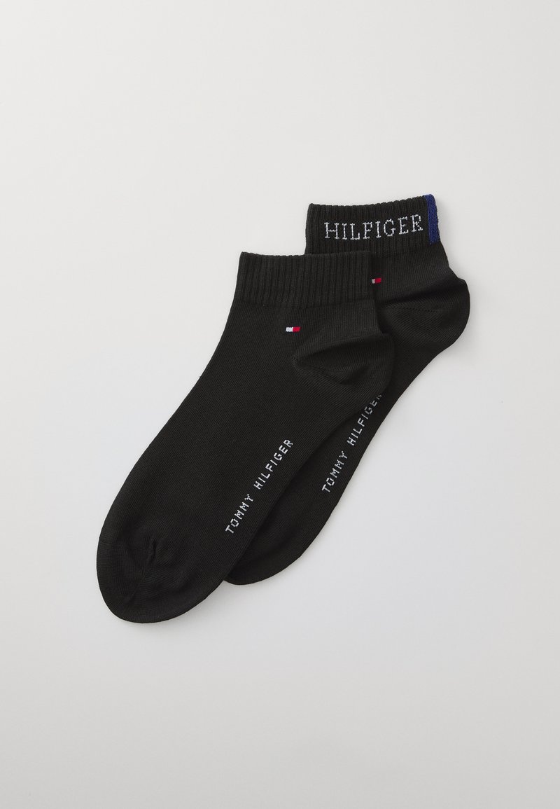 Svarta ankelsockor gjorda av mjukt tyg, med en ribbad kanten som har texten "HILFIGER" och en färgad accent, samt subtil branding på sidan.