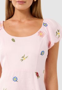 Vaaleanpunainen mekko lyhyillä puffi-hihoilla, jossa on brodeerattuja kukkakuoseja eri väreissä. Pehmeä kangas ja avonainen kaula-aukko.