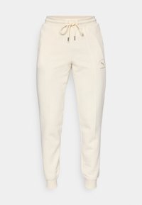 Pantalons de survêtement de couleur crème en tissu doux, dotés d'une taille élastique avec cordons de serrage et de poignets côtelés. Comprend un détail de logo subtil.