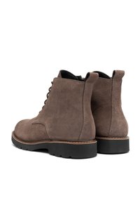 Botas de tobillo de ante marrón con puntera redondeada, parte delantera con cordones y suela de goma negra en contraste. Diseñadas con detalles de costura y una lengüeta.