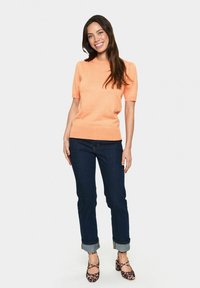 Maglione corto a maniche corte color arancione chiaro con scollo rotondo, abbinato a jeans blu scuro con risvolto e scarpe con tacco a blocco con stampa leopardata.