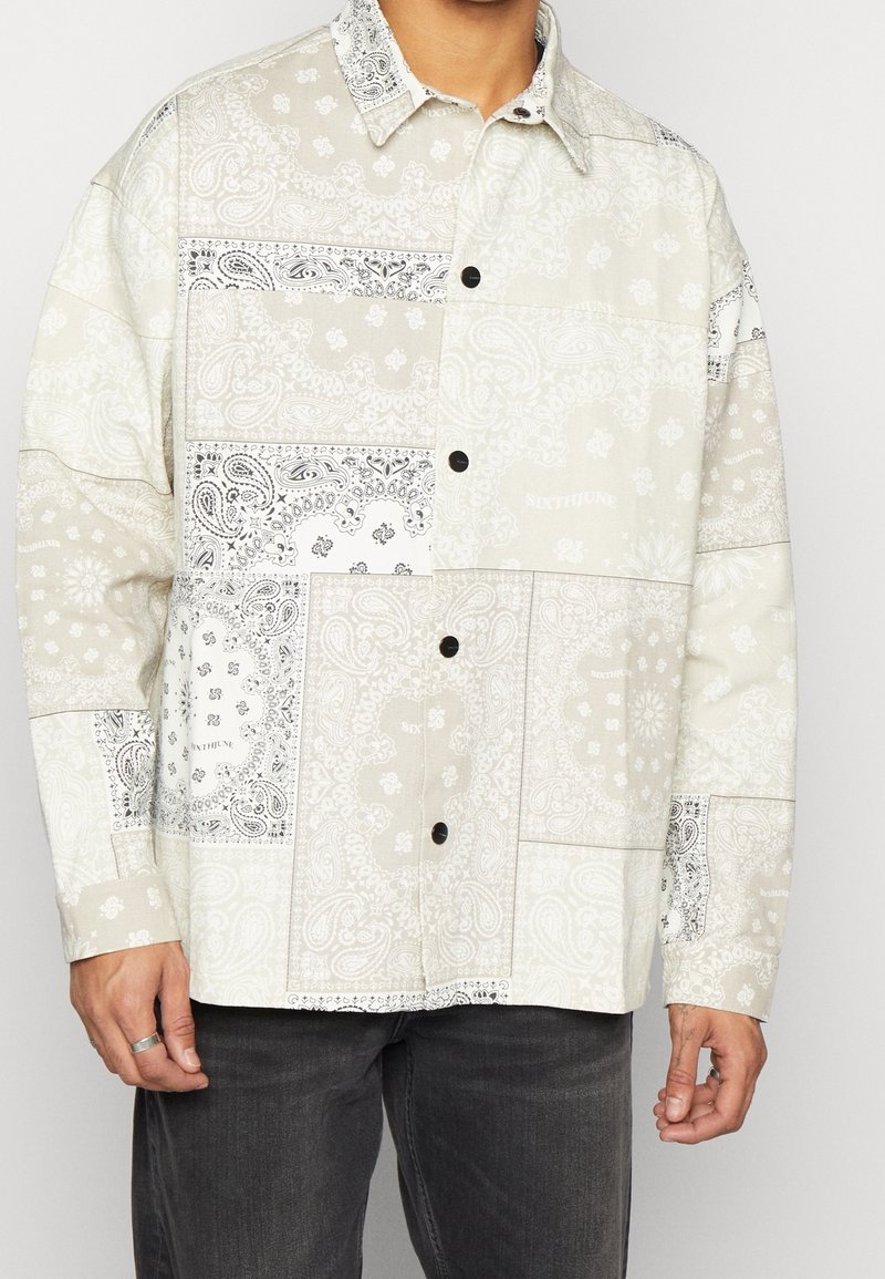 Camicia a maniche lunghe di colore chiaro con motivi paisley in bianco e nero, dotata di colletto e vestibilità rilassata.