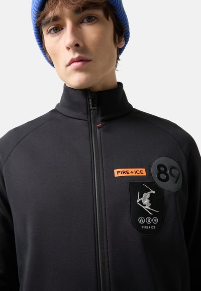 Black jacket with high collar, front zipper, orange "FIRE+ICE" patch, and circular logo. Features skiing graphics and textured fabric.