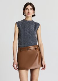 Pull sans manches gris en maille torsadée associé à une minijupe en cuir synthétique marron avec une taille ceinturée, une texture lisse et un léger éclat.
