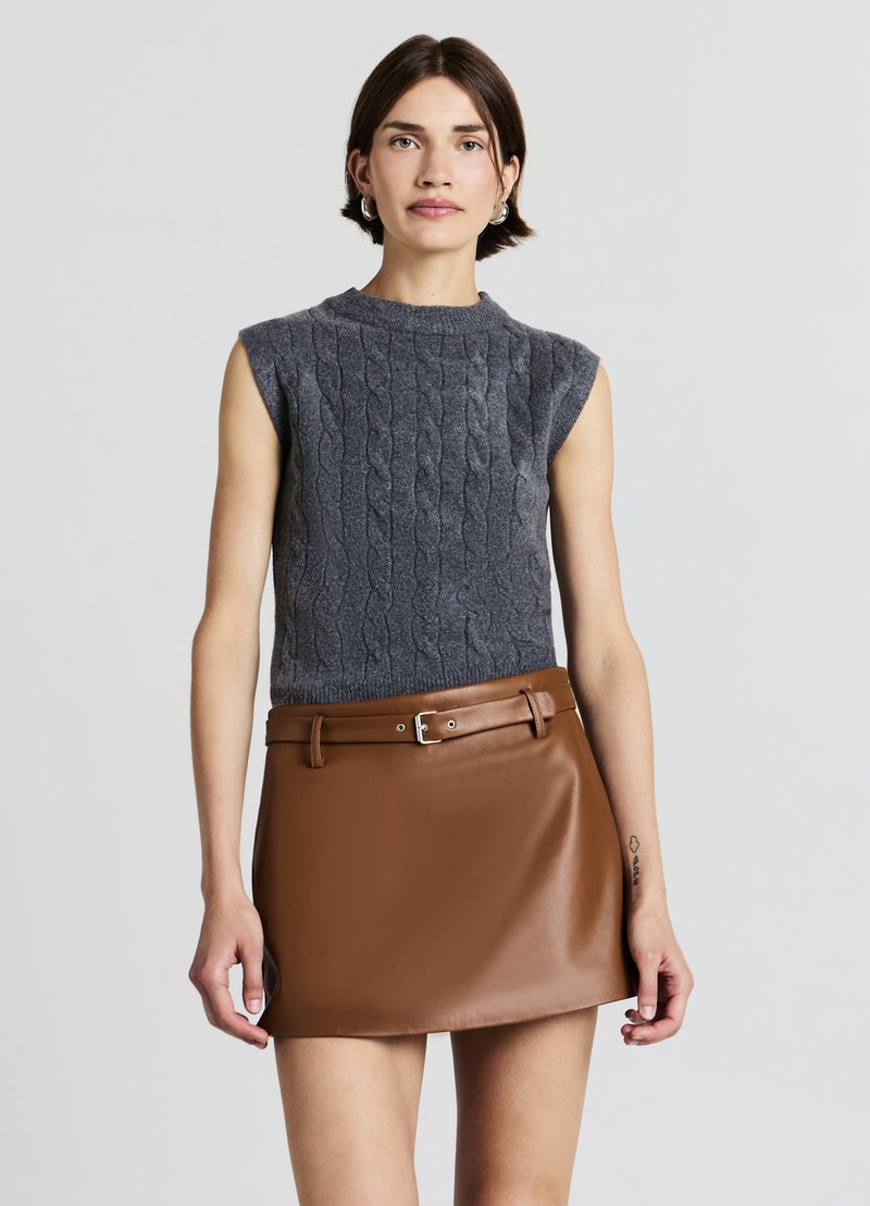 Pull sans manches gris en maille torsadée associé à une minijupe en cuir synthétique marron avec une taille ceinturée, une texture lisse et un léger éclat.